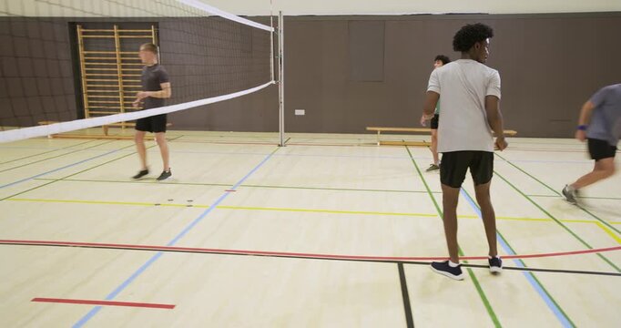 Diverse male teammates reacting to ball from left, blocking and redirecting at net during practice