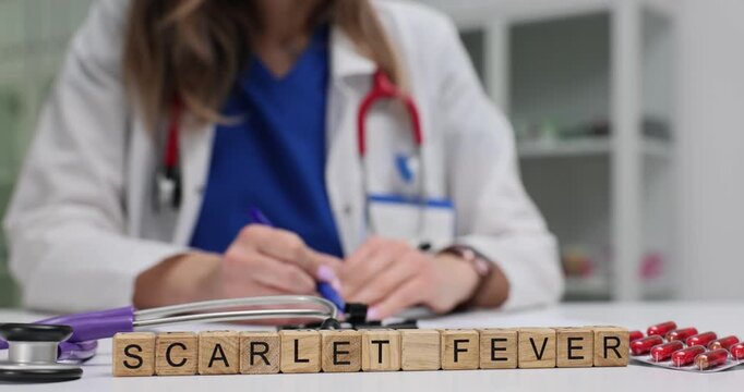 Wooden blocks spell phrase Scarlet Fever near stethoscope and red tablets. Doctor woman fills patient form tracking fever rash symptoms daily