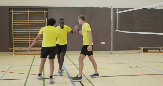 Three male players in yellow shirts celebrating after opponent failing to return ball spike at gym