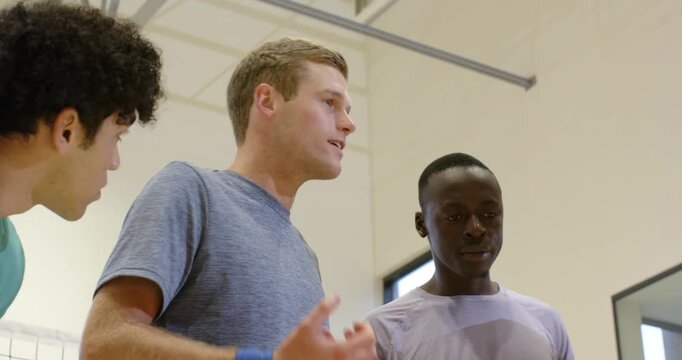 Diverse male team heeding speaker gesturing, stacking hands in gym in tees with wristband for pep