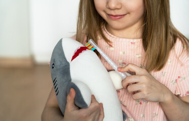 Close up of little girl brushes teeth of toy shark. Childrens hands with toothbrush. Baby milk teeth change. Oral hygiene. Health care