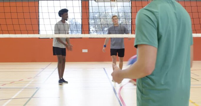 Diverse male players near net receiving green shirt serve, redirecting volleyball during gym drill