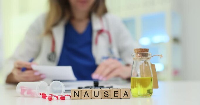 Wooden blocks spell word Nausea near medicine bottle and capsules. Doctor woman reviews dosage card tracking stomach reaction after treatment
