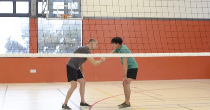 Diverse male team in shorts huddling in gym leading setter lifting ball over net starting rally