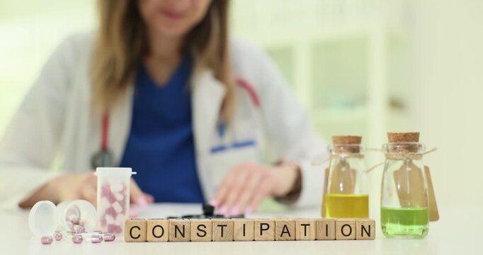 Wooden blocks spell word Constipation near herbal bottles and tablets. Doctor woman explains bowel problem planning diet change and laxative use