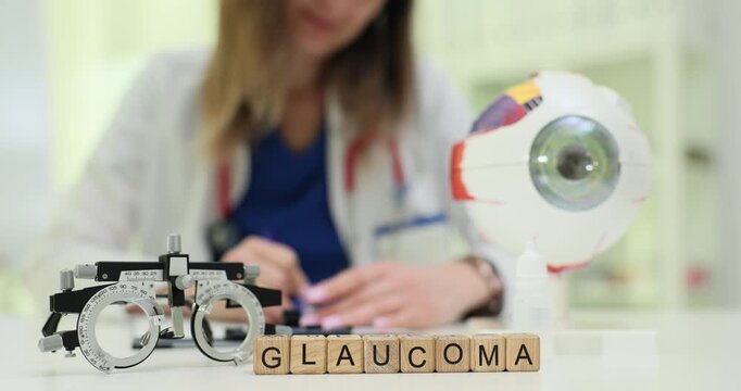 Wooden blocks spell word Glaucoma near eyeball model and medical goggles. Doctor woman records vision test preparing pressure screening for patient