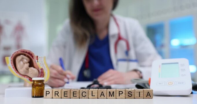 Wooden blocks spell word Preeclampsia near fetus model and blood pressure monitor. Doctor woman notes signs tracking pressure for pregnancy care