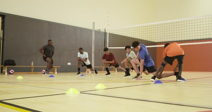 Coach in orange demonstrating forward lunge, training male players doing lunges on court with cones
