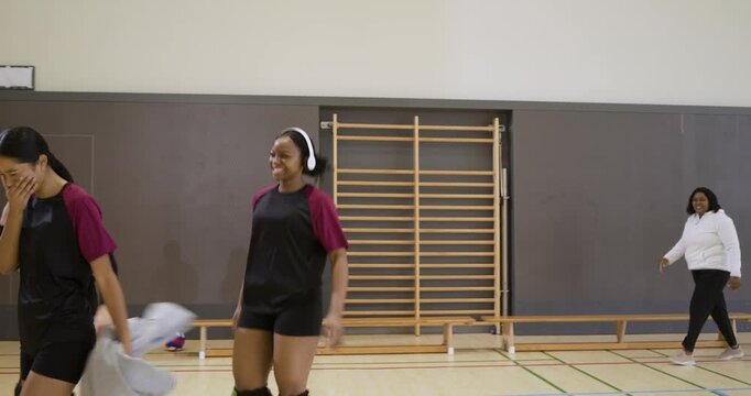After play, female volleyball players walking on court past net in maroon kits, coach clapping