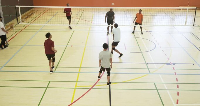 Two opposing diverse male volleyball teams trading serves and spikes in gym practicing ball control
