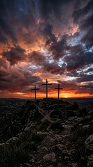Obraz premium Silhouettes of three crosses on a hill at sunset with vibrant clouds creating a dramatic atmosphere.
