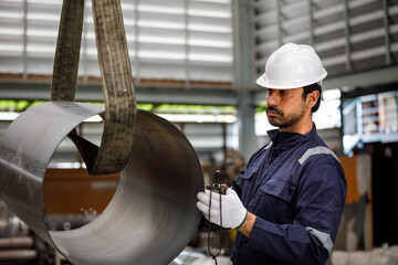 Factory workers use a crane to lift large metal pipes in the factory, demonstrating the use of heavy machinery, safety, and precision in manufacturing.