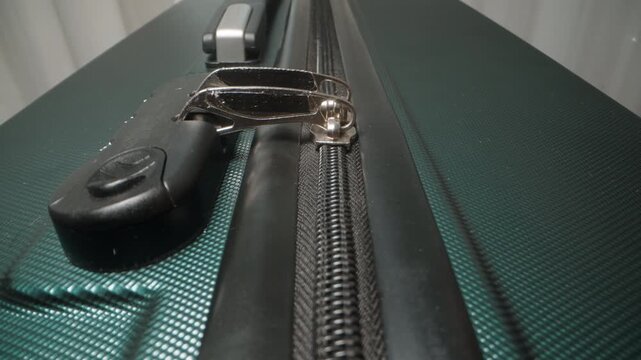 A Hand pulls the zipper closed on the suitcase, securing the contents before locking it with the combination lock.
