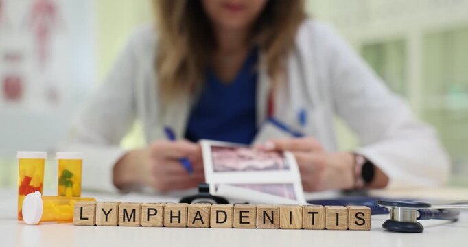 Wooden cubes arranged on table to form word Lymphadenitis. Female doctor attentively studies ultrasound images evaluating possible abnormalities