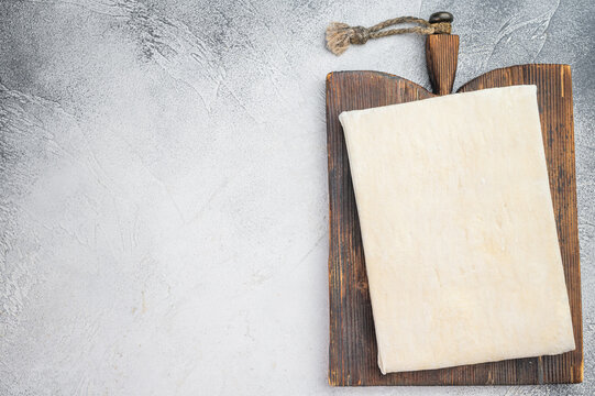 Puff pastry dough sheet on wooden board, raw baking ingredient on rustic background with copy space
