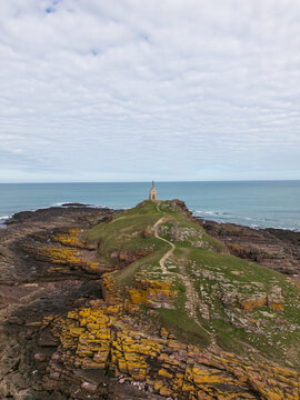 Aerial view of the rugged coastline with a path leading to a stone structure against the backdrop of the sea, Erquy, France.
