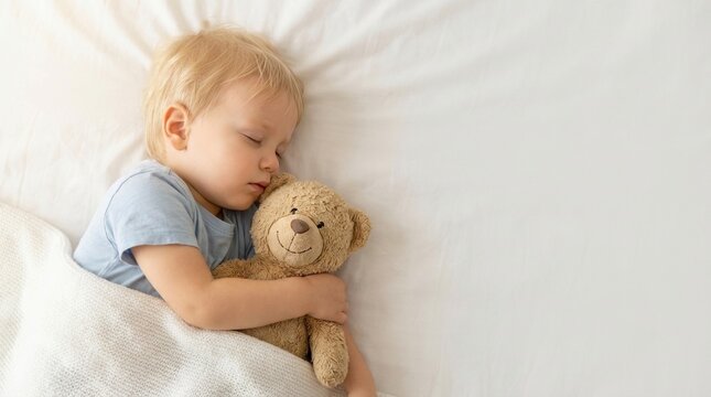 close-up overhead of sleeping toddler hugging teddy bear on bed with soft lighting and negative space. concept of tranquility, rest, daily routine, and bedtime ritual