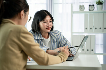 Obraz premium Two women collaborate at a desk with a laptop , Scene is one of collaboration and communication`