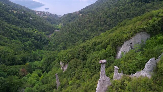 Drone over Zone earth pyramids (Piramidi di Zone) Lake Iseo in Lombardy Italy, glides above hoodoo capstones and clay spires revealing a deep green gorge and eroded cliffs