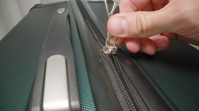 A Hand zips up the suitcase and secures the zipper pulls in the lock, finalizing preparations before heading out on a journey. Dolly slider, close up.