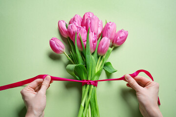Woman hands tying pink ribbon on tulips, Mother's Day
