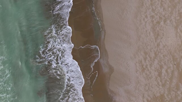 Top view drone footage of the Caspian Sea coastline showing turquoise waves rolling onto an empty sandy beach peaceful and natural coastal scene with clean shoreline and gentle wave motion