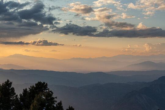 View of hazy mountain ranges fading into the horizon under a sky streaked with golden light and dramatic clouds, Arang Kel, Azad Kashmir, Pakistan.