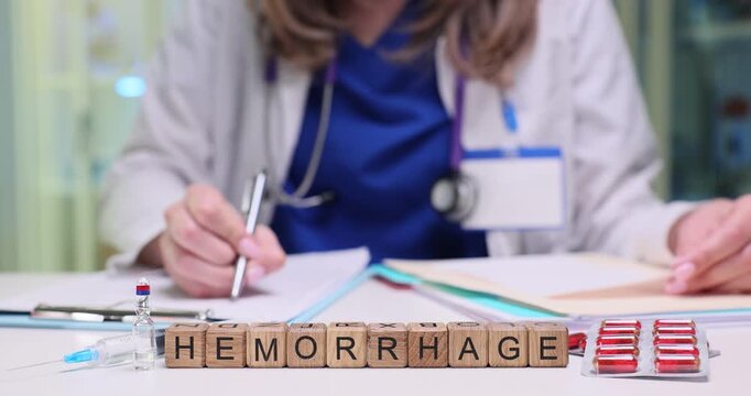 Wooden blocks spell word Hemorrhage near documents and medicine packs. Doctor writes notes reviewing patient case details to manage bleeding risk