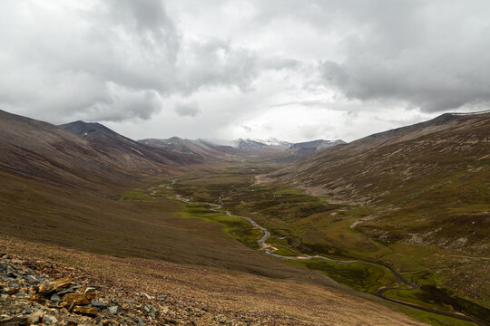 Aerial view of winding river snaking through stark, rugged terrain under a moody, overcast sky, Babusar, KPK, Pakistan.