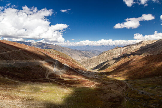 Aerial view of rugged mountains with winding roads carving through the landscape under a bright sky with scattered clouds, Babusar, KPK, Pakistan.