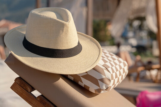 Straw hat resting on lounge chair at a beachside terrace with soft sunlight, relaxed summer atmosphere, coastal resort setting with a cabana and blurred background tranquillity
