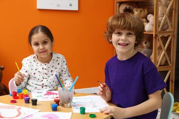 Obraz premium Portrait of happy little friends drawing together with brushes and paints at table indoors