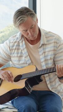 Vertical video: Settling guitar, man in shirt practicing plucking and strumming by window with tabs