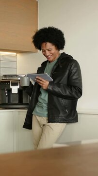 Vertical video: Looking at tablet, man in jacket tapping tablet in kitchen, holding mug by maker