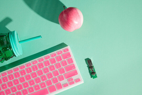 USB board, pink keyboard, green cup with straw and pink apple on mint background, remote work and healthy snack concept, copy space
