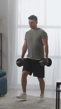 Young man performing dumbbell exercise at home in bright living room, focusing on strength training, balance, and controlled lower body movement with free weights