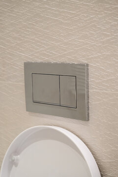 Modern toilet flush system in a bathroom, featuring a chrome dual flush plate for water saving and efficient sanitary technology