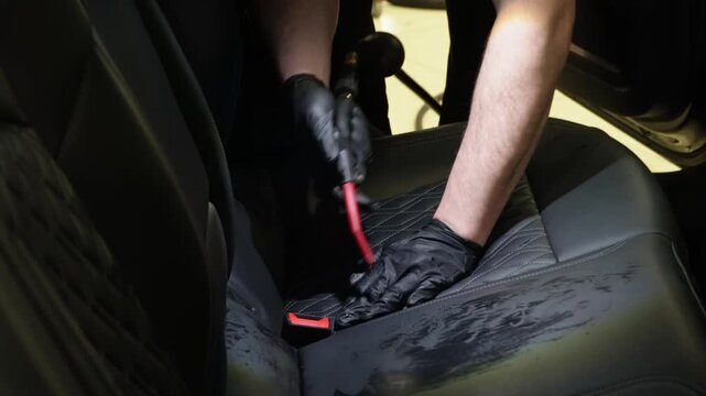 Dry cleaning of the car interior, close-up, selective focus. Car detailing, the concept of car interior care. The detailing master cleans the car interior with a hot steam cleaner, brush, microfiber.