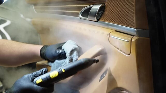 Dry cleaning of the car interior, close-up, selective focus. Car detailing, the concept of car interior care. The detailing master cleans the car interior with a hot steam cleaner, brush, microfiber.