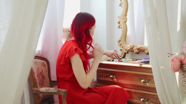 Elegant Red-Haired Woman in Red Dress at Vintage Dressing Table with Mirror Applying Makeup
