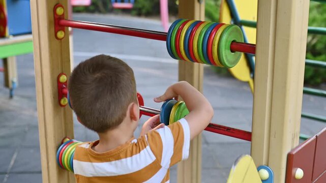 A preschool boy plays on a playground with a colorful wooden abacus, the child learns to count, early development