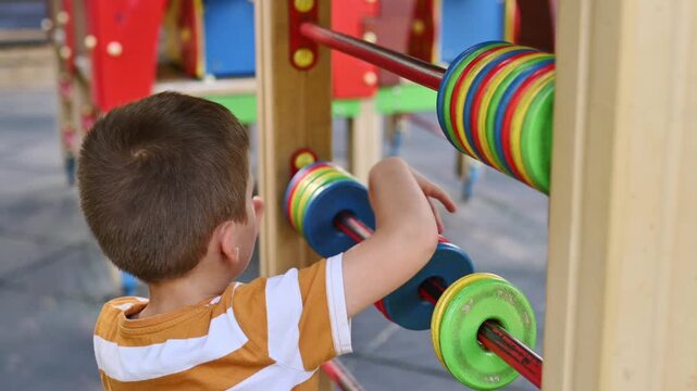 A preschool boy plays on a playground with a colorful wooden abacus, the child learns to count, early development