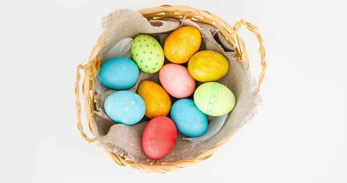 A wicker basket filled with colorful Easter eggs. The Easter arrangement is on a white surface, top view. Looped 4K stop motion animation