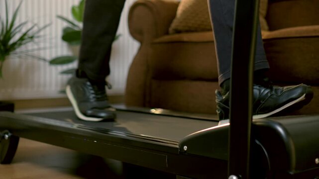 Rapid treadmill walking with unrecognizable runner maintaining brisk pace during indoor cardio workout at home. Close view of legs stepping quickly across moving belt while sustaining steady training