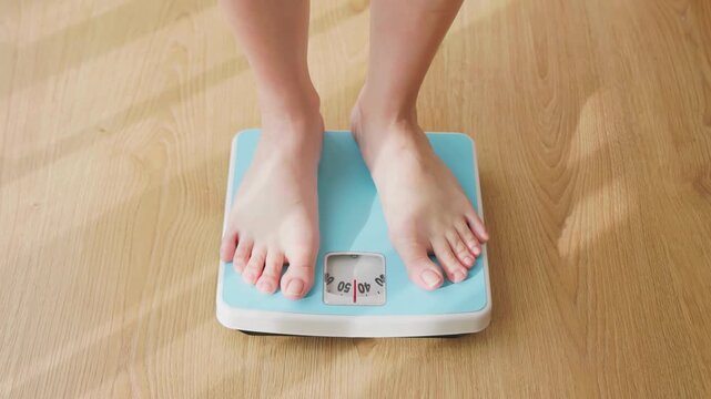 Barefoot woman stepping on a light blue bathroom scale indoors