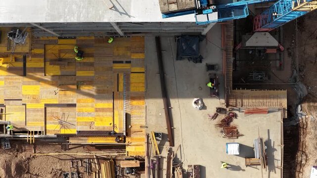 Aerial drone shot looking straight down at two construction workers installing steel reinforcement on formwork deck, showcasing structural preparation and active building process.