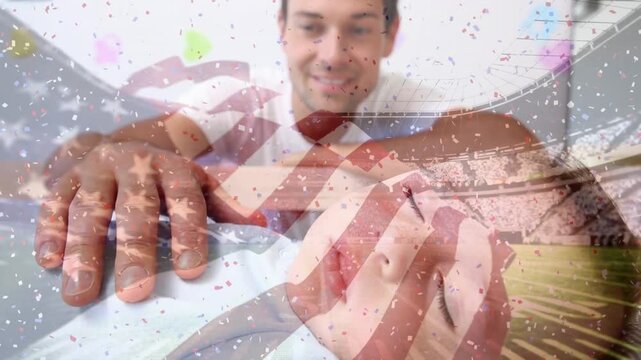 Animation of flag of usa, confetti and stadium over happy caucasian father watching baby sleeping
