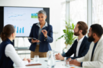 Fototapeta premium soft focus blurred photo of Professional business presentation in modern office, mature female leader speaking to diverse team, corporate meeting with data charts on screen