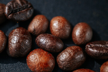 Obraz premium Macro close-up of roasted coffee beans scattered on a dark textured surface, highlighting rich brown tones, an oily sheen, and detailed textures with a shallow depth of field.