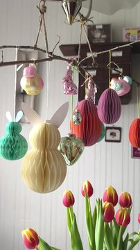 Inspirierende Idee zu Ostern: h&auml;ngender Osterstrauss. Wabenpapier-Hasen und -Eier in Pastellt&ouml;nen sowie gl&auml;serne Vintage-Figuren. Im Vordergrund sind frische rot-gelbe Tulpen.